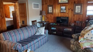 Een gezellig interieur van een chalet met een gestreepte bank, een televisie en ingelijste foto's aan de wanden.