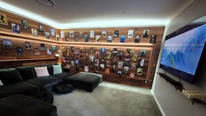 Ein gemütliches Wohnzimmer mit einer großen Wand voller Filmplakate, einem bequemen Ecksofa und einem Flachbildfernseher an der Wand.
