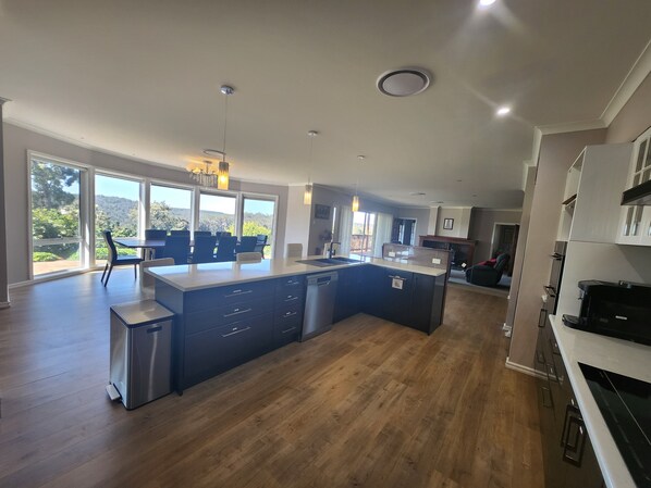 A modern kitchen with a large island, wooden flooring, and large windows offering a view of the outdoors.