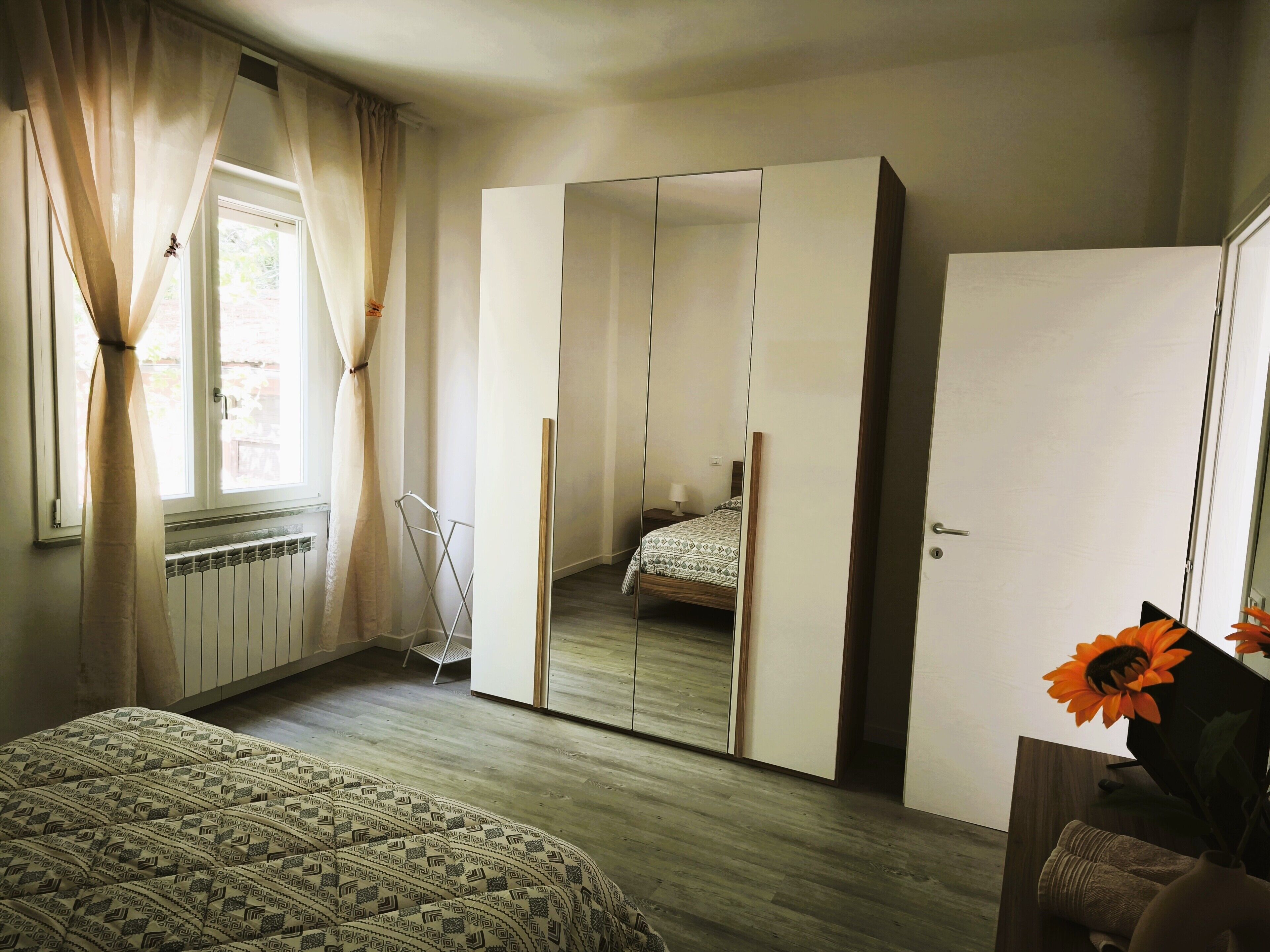 Un dormitori amb un llit, un armari, un radiador i una finestra amb cortines.