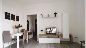 Un comedor moderno con una mesa blanca, sillas y una pantalla de televisión que muestra una escena.