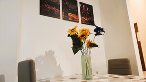Una mesa de comedor con mantel estampado, un jarrón con girasoles y dos cuadros en la pared.