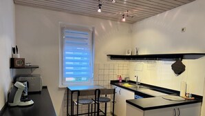 A compact kitchen with a coffee machine, a window with blinds, a sink, and a small dining area. - Apartment in the center with garden, connection to Stuttgart, Märklineum and EWS Arena. (Göppingen)