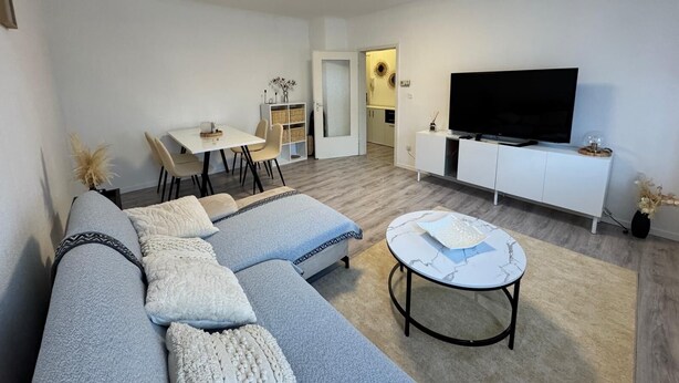 A modern living room with a sofa, coffee table, TV, and dining area. - Apartment in the center with garden, connection to Stuttgart, Märklineum and EWS Arena. (Göppingen)
