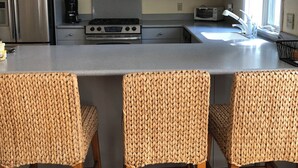 A modern kitchen with grey cabinets, stainless steel appliances, a central island with bar stools, and a wooden floor. - Spacious 4-bedroom house in enjoyable Dewey Beach with WiFi, AC (Dewey Beach)