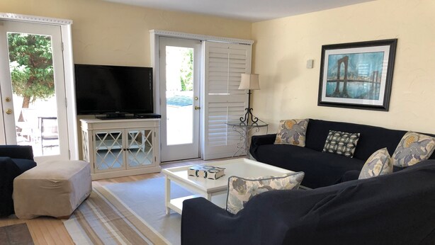 A living room with a black sofa, a white coffee table, a TV on a cabinet, and a door leading outside. - Spacious 4-bedroom house in enjoyable Dewey Beach with WiFi, AC (Dewey Beach)
