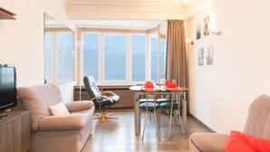 Una sala de estar moderna con un sofá, una mesa de comedor con sillas, un televisor y un ventanal con vistas.
