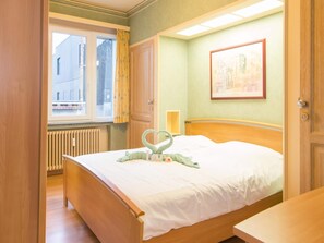 A bedroom with a wooden bed, a window with curtains, a radiator, and a framed picture on the wall. - Sea View Apartment in Ostend (Ostend)