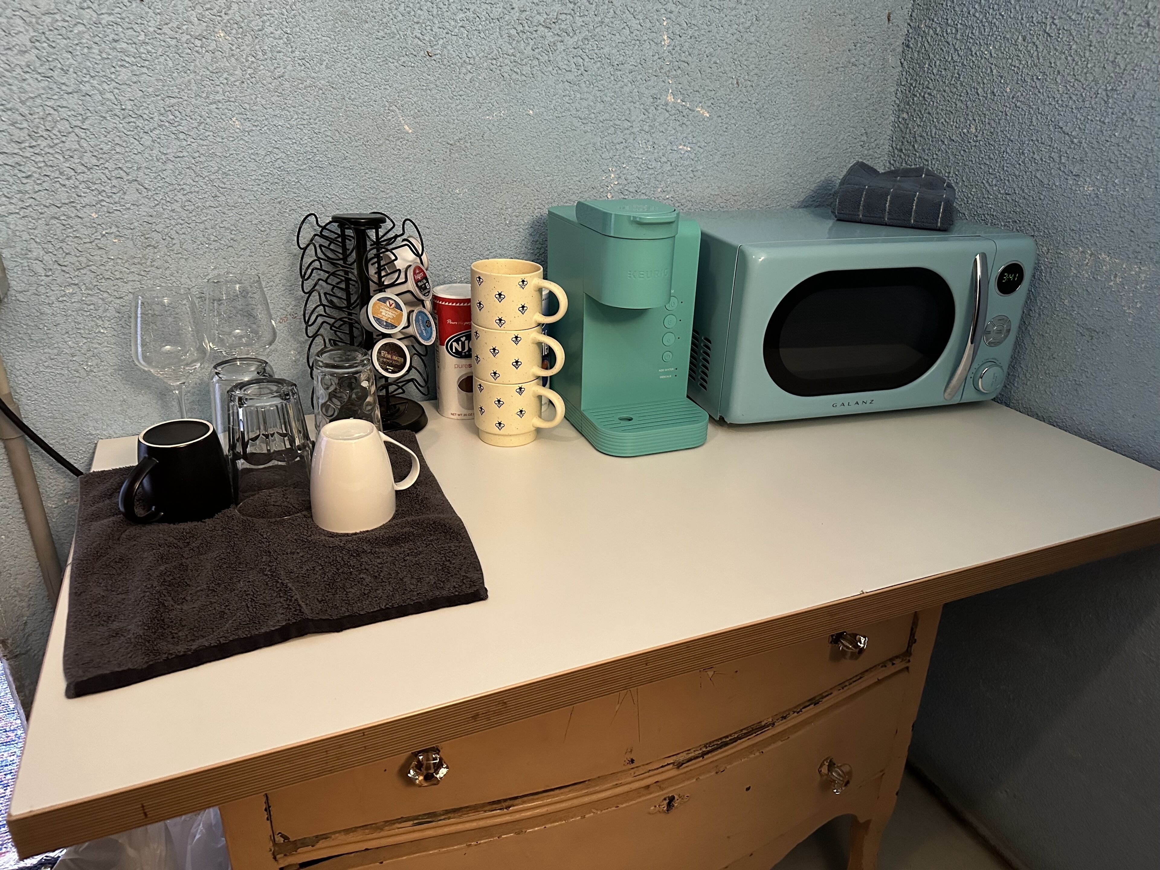 Eine Küchenzeile mit einer Mikrowelle, einer Kaffeemaschine und verschiedenen Tassen auf einer Arbeitsfläche.