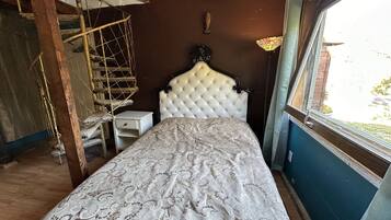 A bedroom with a bed, a small bedside table, a hanging chair, and a window with a view of the outside.