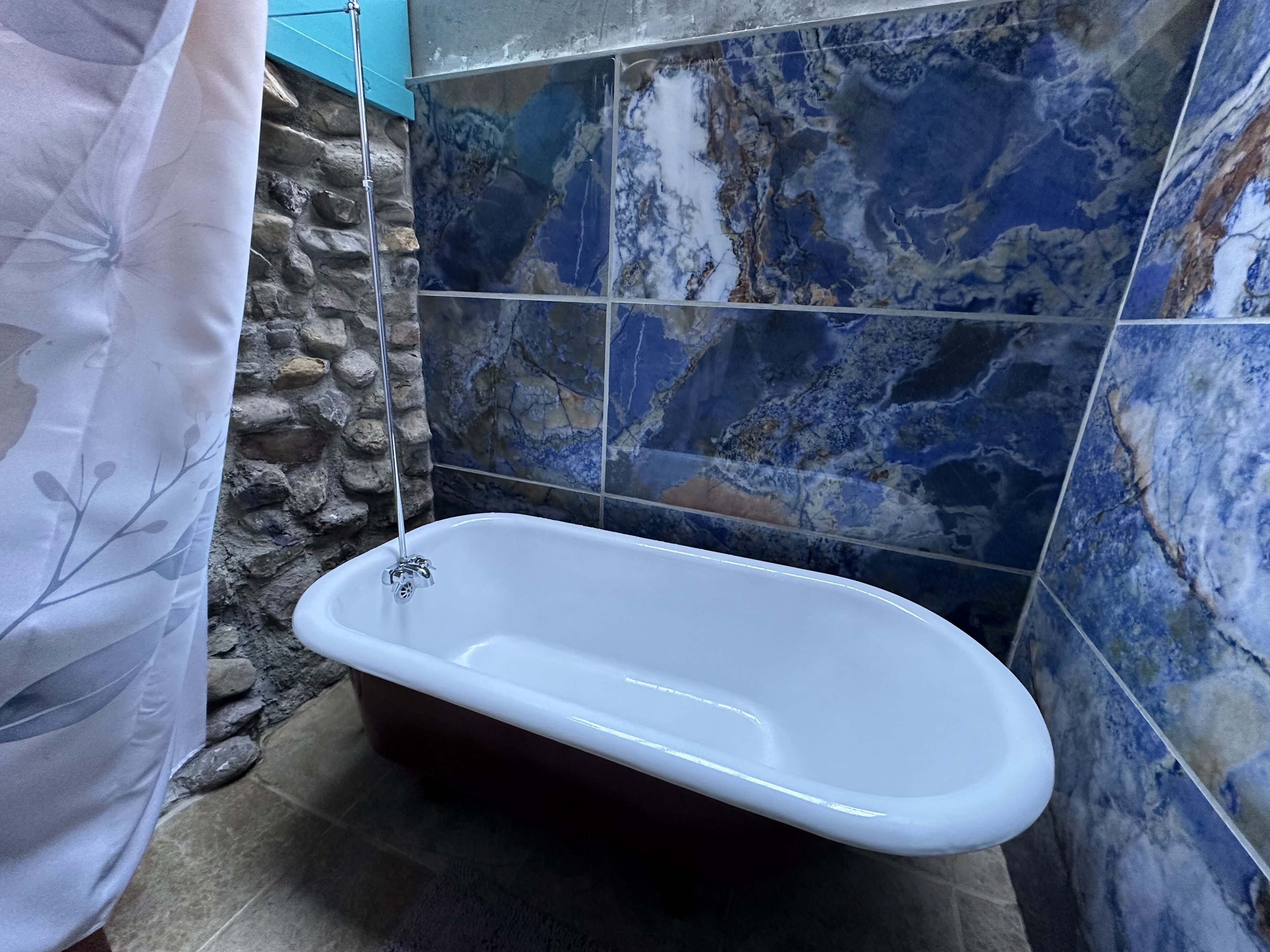 Une salle de bain avec une baignoire sur pieds, un mur en pierre et des carreaux de marbre bleu.