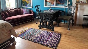 A room with a blue wall, a red sofa, a wooden floor, a table with a lamp, and a colorful rug. - Mermaid Suite + Private Trails, Cave and Creek! (Topanga)