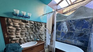A bathroom with a stone wall, a wooden vanity, a freestanding bathtub, and a shower with a curtain. - Mermaid Suite + Private Trails, Cave and Creek! (Topanga)