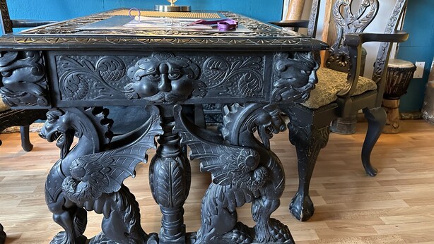 A dark, ornately carved table with a glass top, surrounded by various decorative items and furniture. - Mermaid Suite + Private Trails, Cave and Creek! (Topanga)