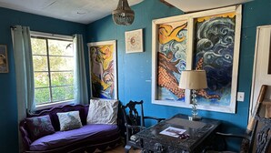 A room with a purple sofa, a wooden table with a lamp, and artwork on the walls. - Mermaid Suite + Private Trails, Cave and Creek! (Topanga)
