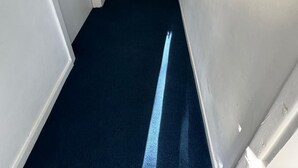 Ein schmaler Flur mit dunklem Teppich und weißen Wänden, der zu einer Treppe führt.
