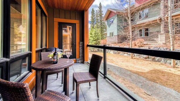 A balcony with wicker furniture and a bottle of wine, overlooking a residential area with houses and trees.
