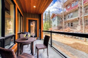 A balcony with wicker furniture and a bottle of wine, overlooking a residential area with houses and trees. - C111- Canmore Plunge- A/C, Hot tub, Pool, Free Parking, 2BR, Sleeps 6 (Canmore)