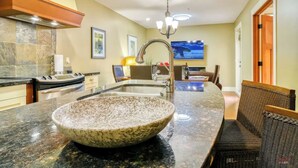A kitchen with a large granite island, a built-in oven, and a stainless steel range hood.
