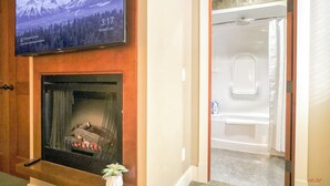 A hotel room with a fireplace, a television mounted above it, and a shower area visible through an open door.