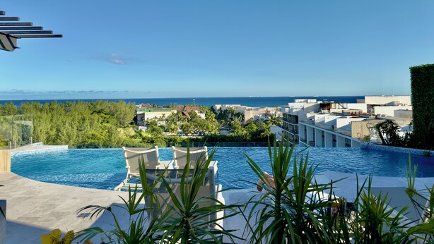 A swimming pool with lounge chairs, surrounded by greenery and buildings, overlooking a coastal area. - Sea Tower by Casago (Playa del Carmen)