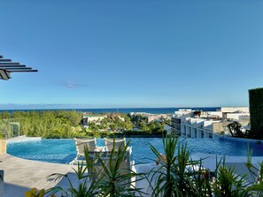 A swimming pool with lounge chairs, surrounded by greenery and buildings, overlooking a coastal area. - Sea Tower by Casago (Playa del Carmen)