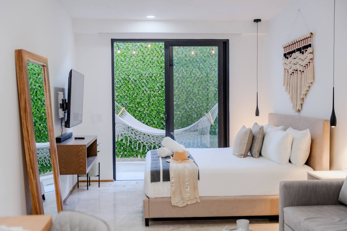 A modern bedroom with a large bed, a desk, a TV, and a hammock by the window.