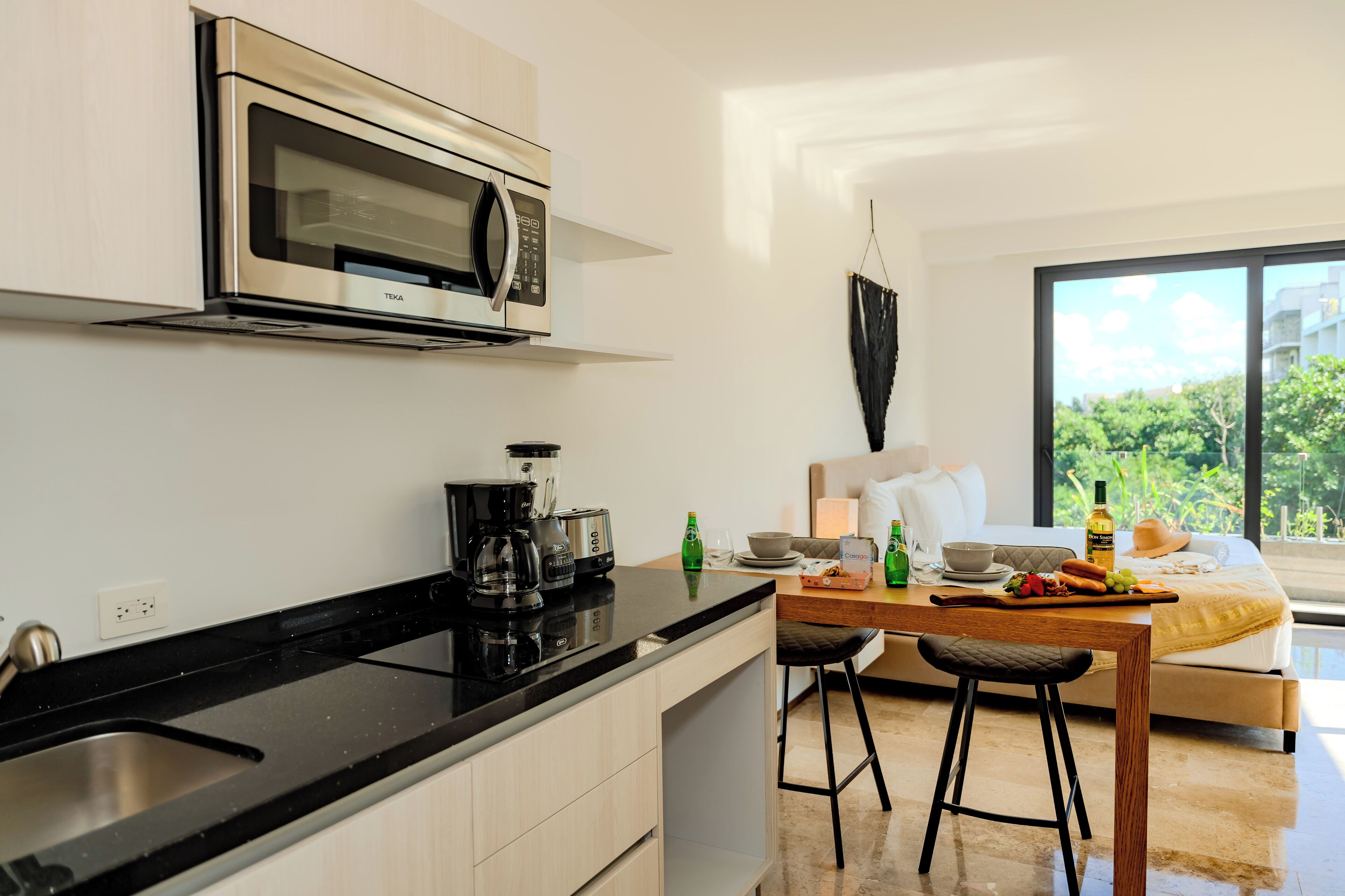Una cucina moderna con forno a microonde, macchina da caffè e sgabelli da bar. C'è un tavolo da pranzo con una colazione servita e un'ampia finestra che si affaccia sul verde.