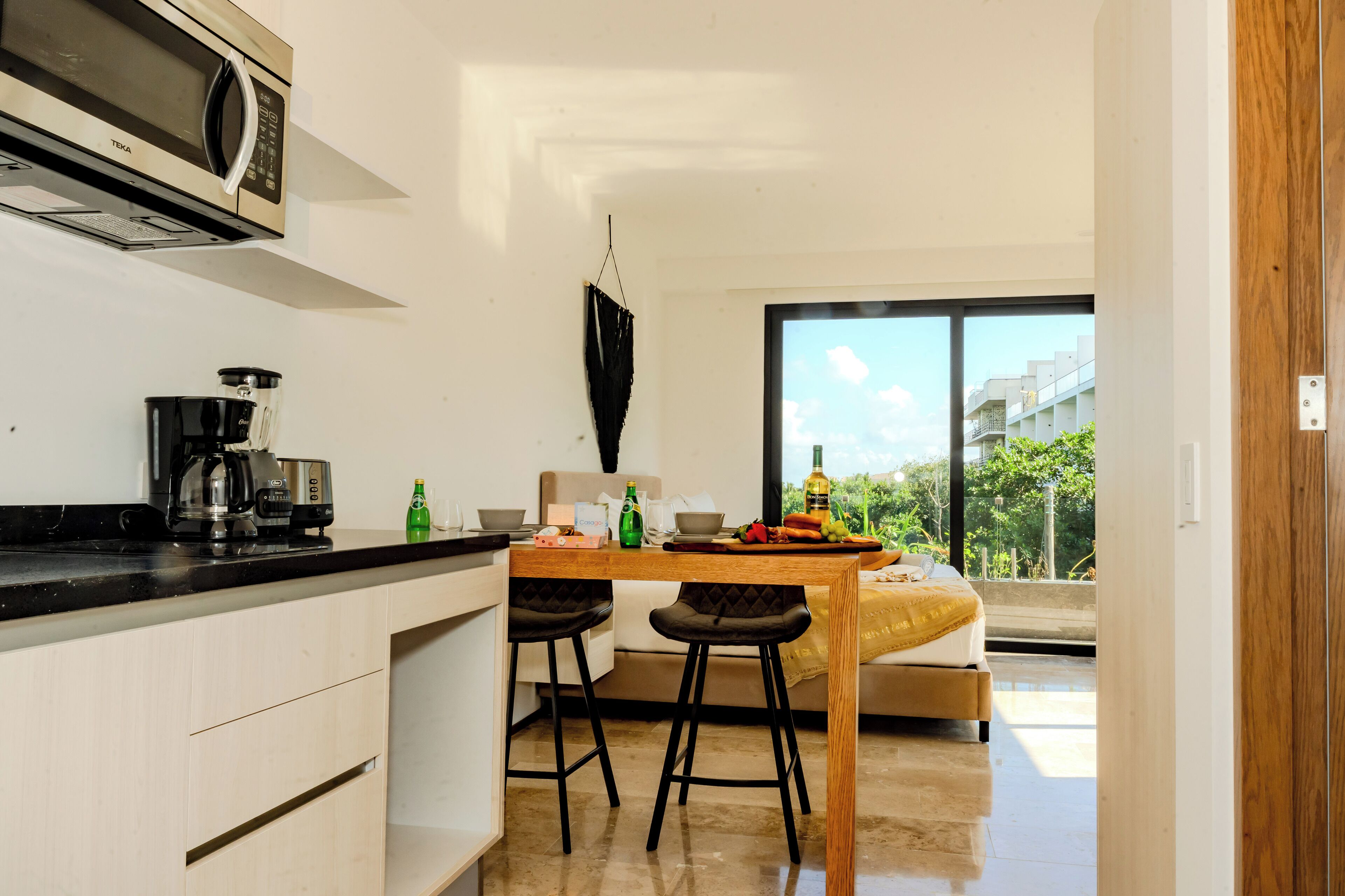 Una cucina moderna con forno a microonde, macchina del caffè e sgabelli da bar. C'è un tavolo da pranzo con un cuscino giallo e vista all'esterno tramite ampie finestre.