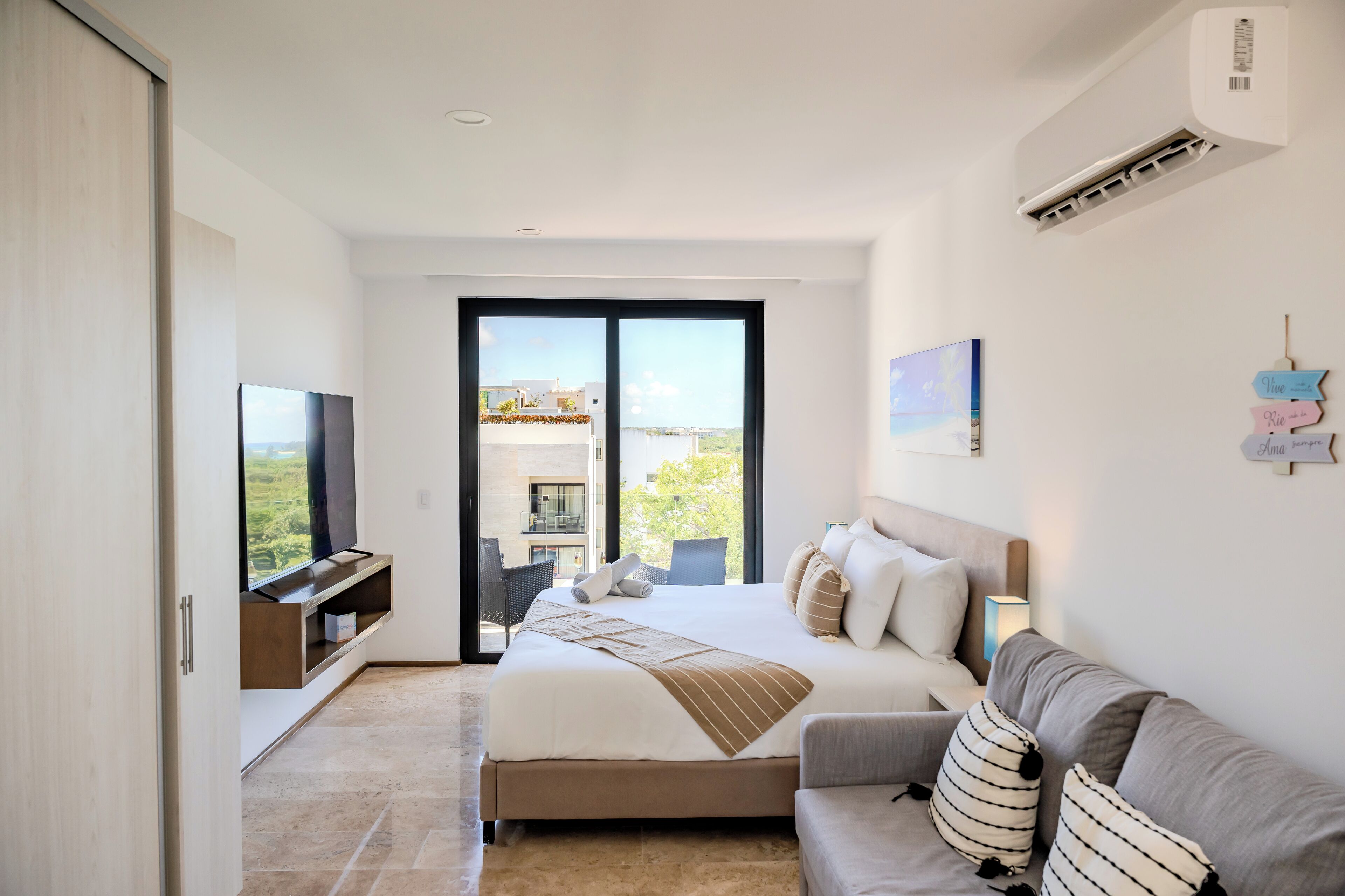 Quarto moderno com cama grande, sofá, televisão e varanda com vista.