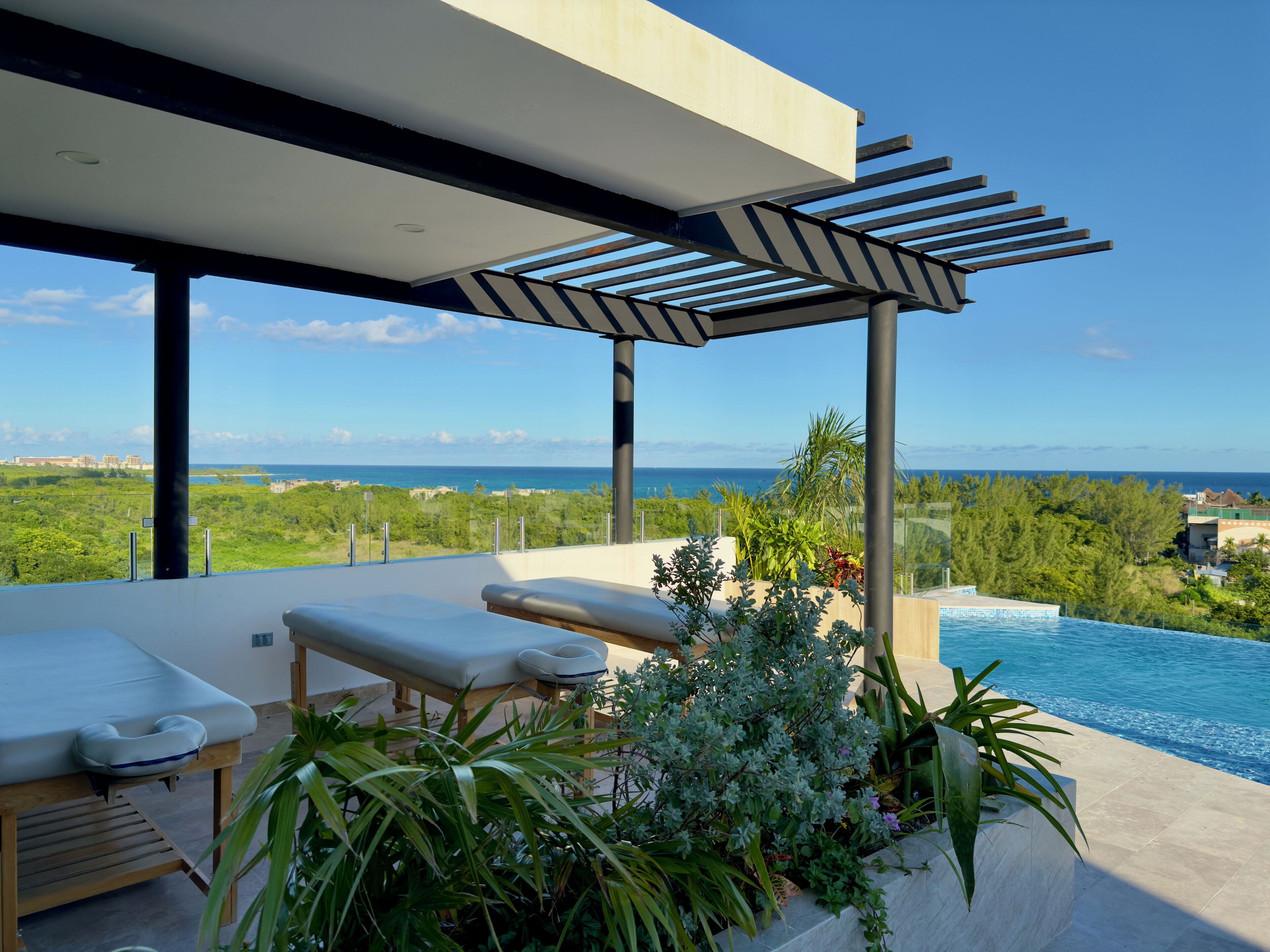 Un espace de détente extérieur moderne avec piscine, comprenant une pergola, des chaises longues et une vue sur l’océan.