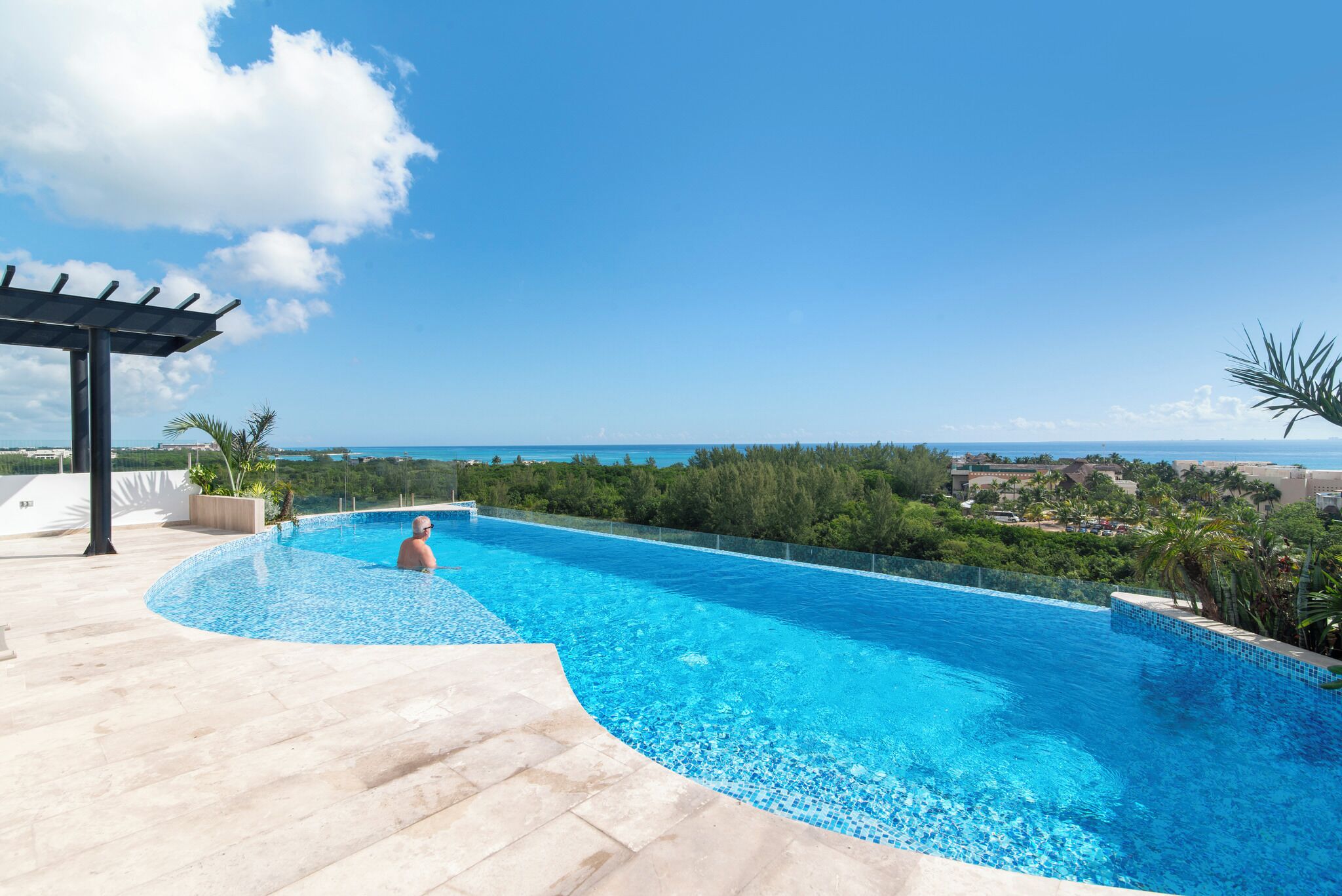 A swimming pool with a curved edge, surrounded by a tiled deck and a pergola.