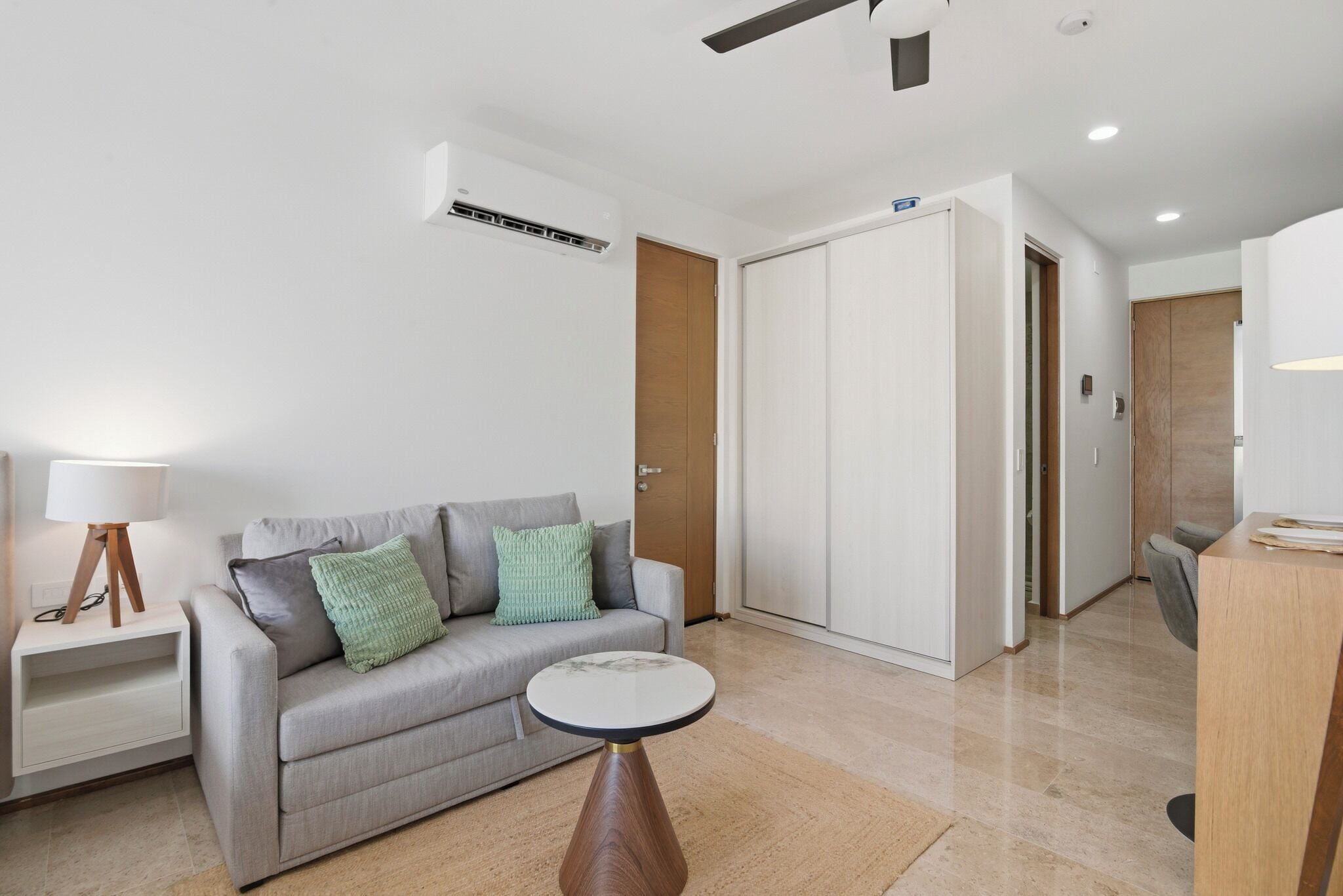 Una sala moderna con un sofá gris, una mesita redonda, una lámpara y un armario.