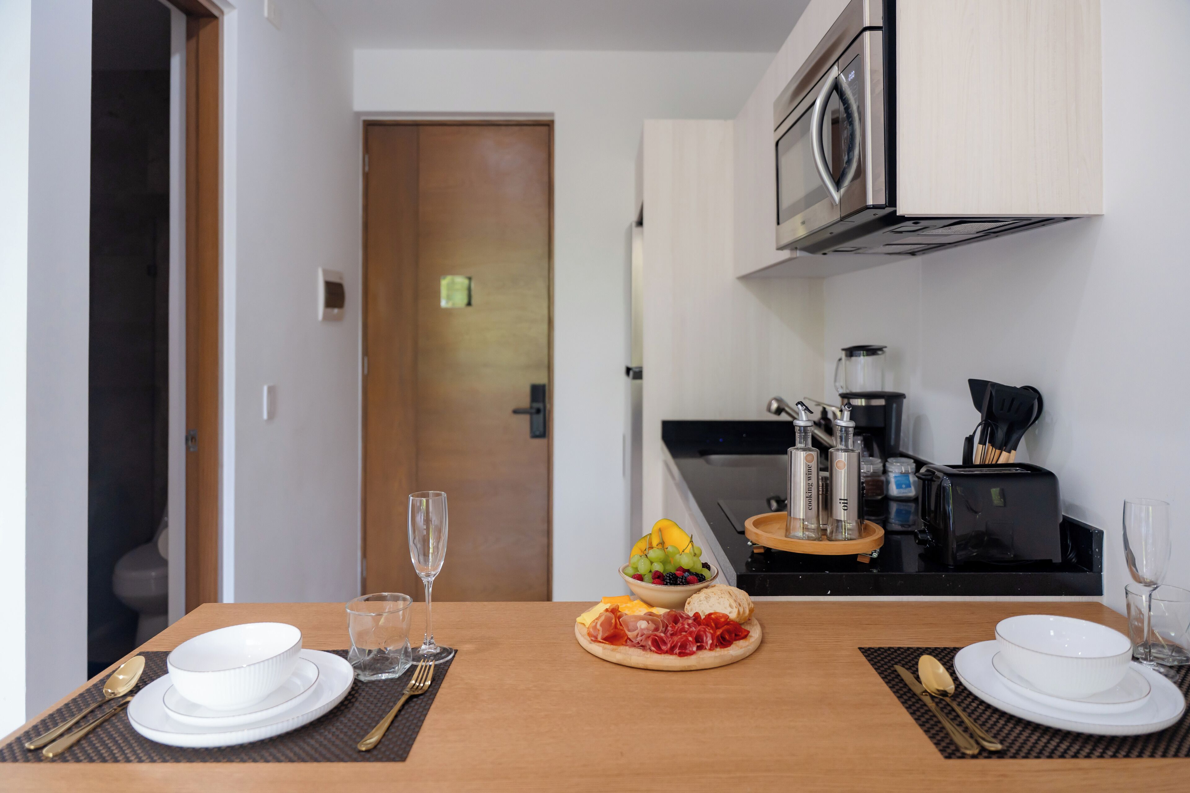Une table à manger dressée avec des assiettes, des couverts et un panier de fruits.