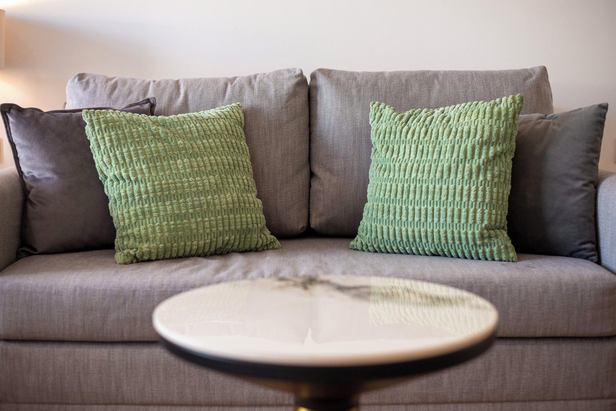 A grey sofa with two green pillows and a round table in front.