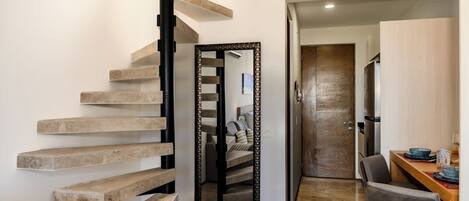 A modern interior with a spiral staircase, a dining area, and a mirrored wall reflecting the staircase.