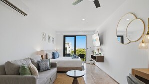 A modern hotel room with a bed, a sofa, a small table, a TV, and a balcony with a view. - Sea Tower by Casago (Playa del Carmen)