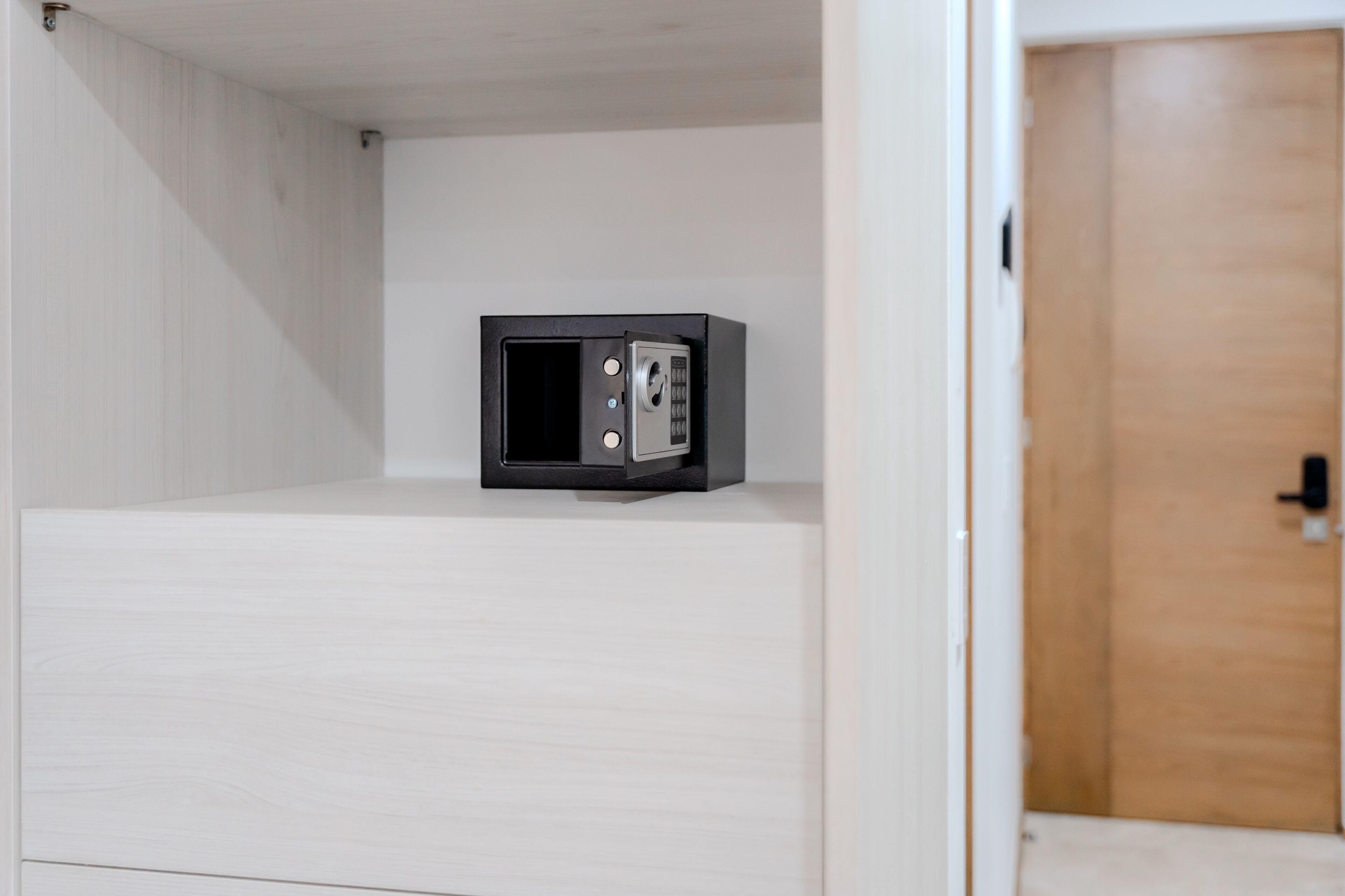 Een kleine, zwarte kluis op een witte houten vloer in een kamer met witte wanden en een houten deur.
