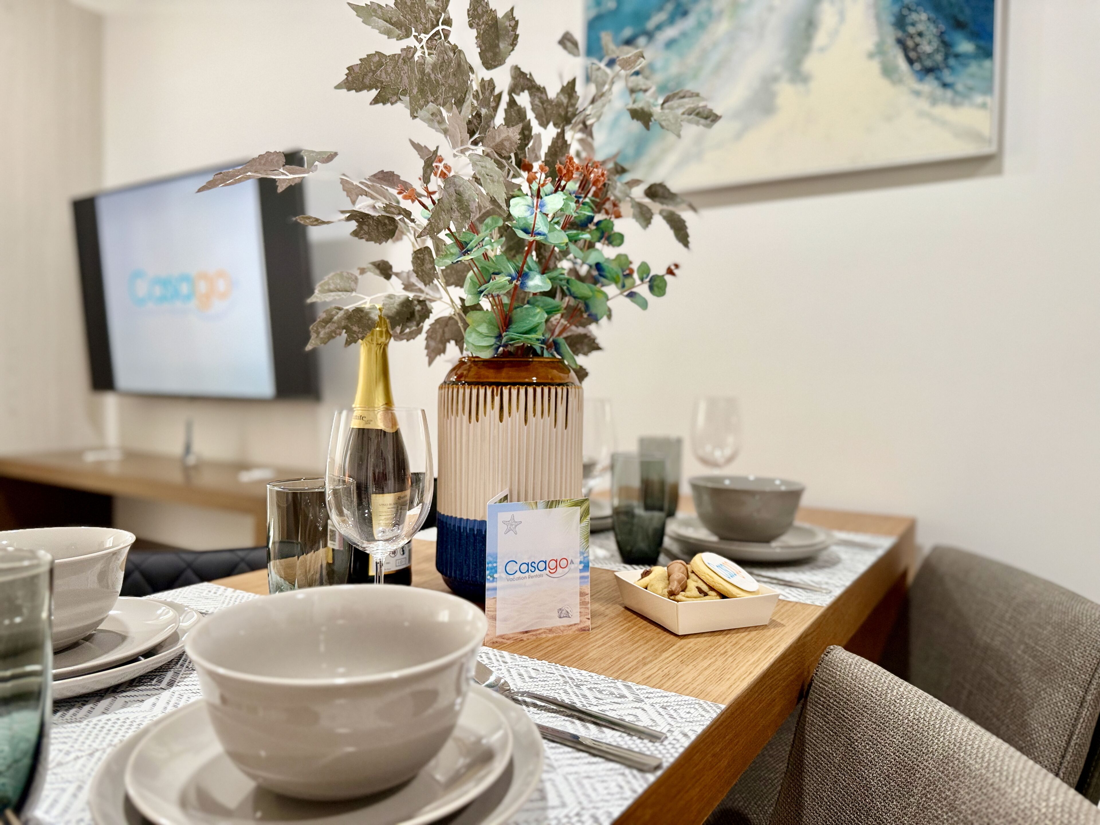 Une table à manger dressée avec des assiettes, des bols, des verres et un vase contenant des fleurs artificielles.
