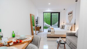 A modern hotel room with a dining area, a bed with a hammock, and a large window with a view of greenery. - Sea Tower by Casago (Playa del Carmen)
