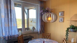 A dining area with a round table, chairs, a hanging light fixture, and a window with curtains. - Complete Apartment With own Balcony (Vohenstrauss)