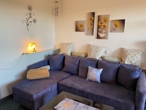 A living room with a sectional sofa, a small table, and wall art. - Complete Apartment With own Balcony (Vohenstrauss)