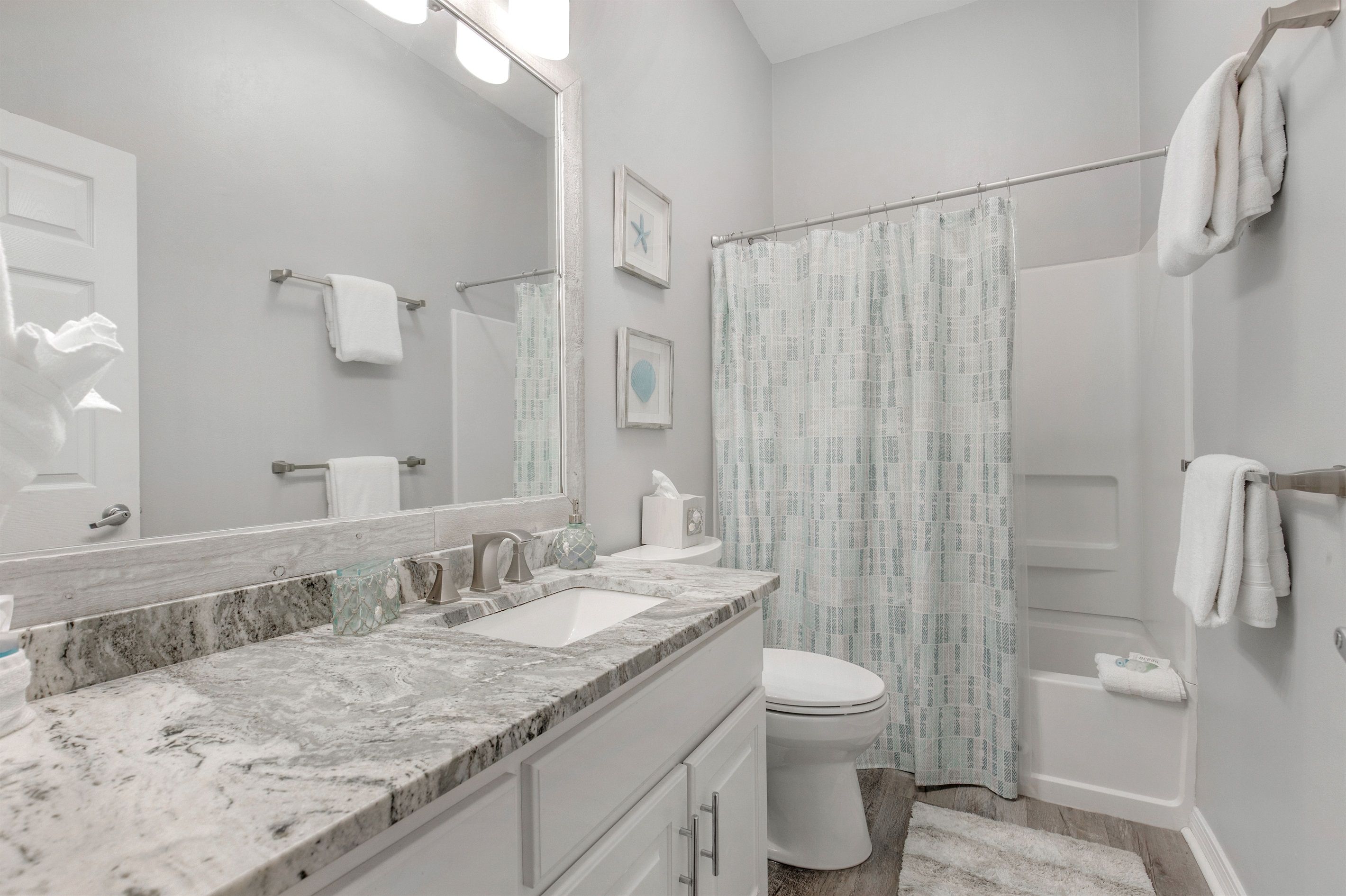 A bathroom with a marble sink, a toilet, a shower with a patterned curtain, and a towel rack.