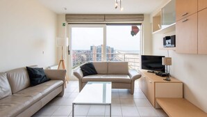 A modern living room with a sofa, a coffee table, and a TV on a stand. - Apartment With Terrace and sea View in Mariakerke (Ostend)