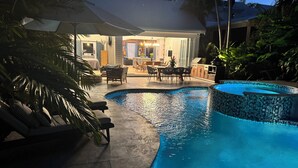 Una piscina con borde de azulejos, rodeada de sillas de descanso y un área de terraza cubierta.