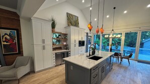 Una cocina moderna con una isla grande, armarios blancos y un comedor con mesa y sillas de vidrio.