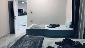 A small, compact bedroom with two beds, a visible kitchenette in the background, and a door leading to another room.