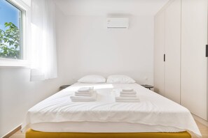 Relax in a serene space with a neatly made bed, bedside table, and natural light pouring in through the window.