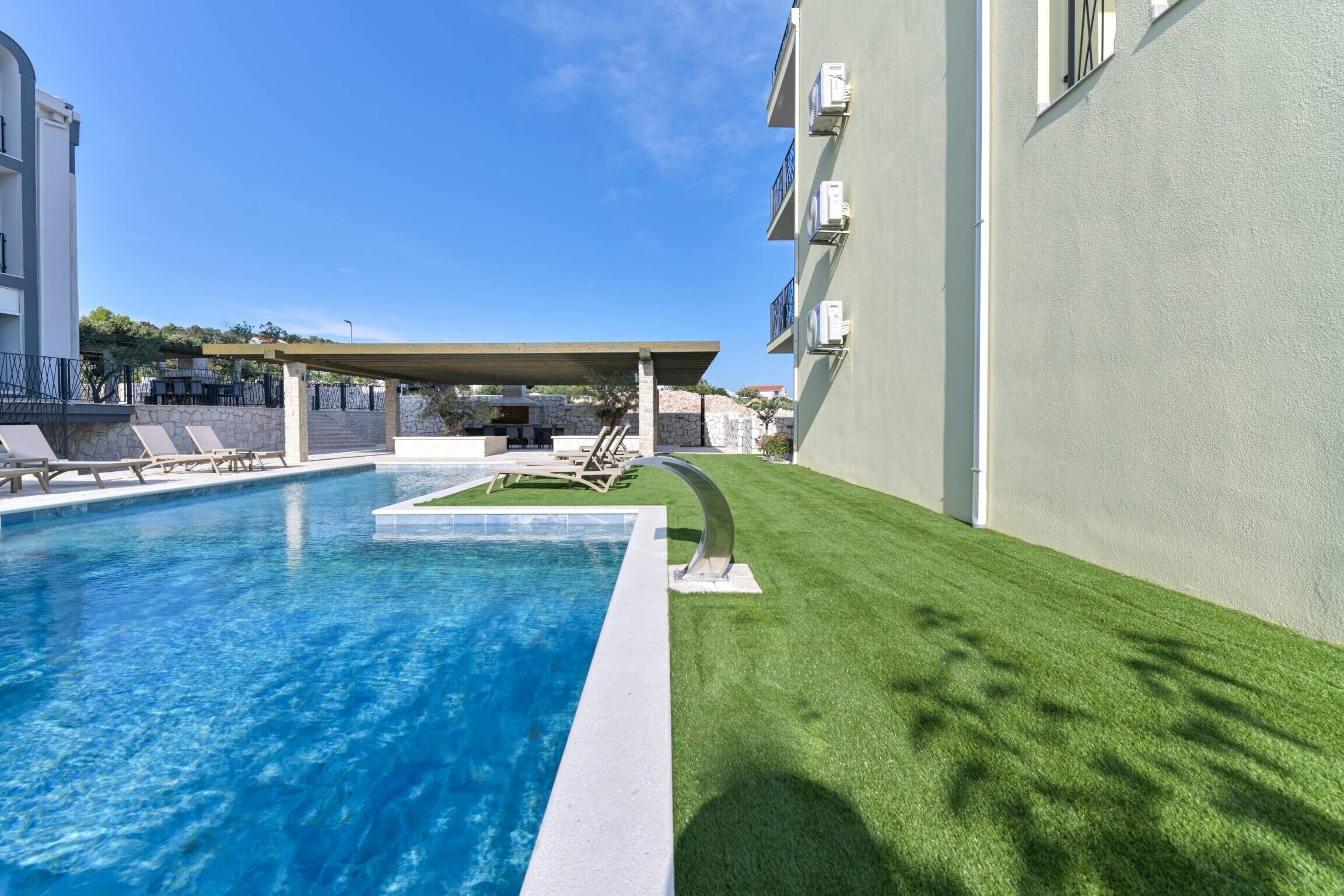 A swimming pool with lounge chairs, a covered seating area, and a well-maintained lawn.