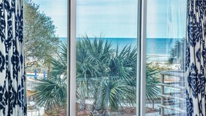 Habitació amb una finestra gran que ofereix vistes a la platja i palmeres.